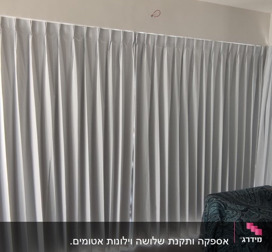 וילון לבן תלוי על מסילה בחדר מואר